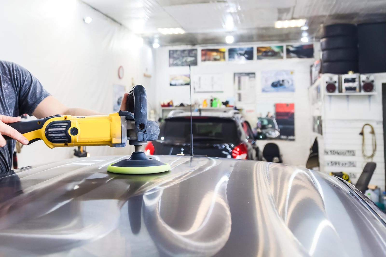 Detalhista utiliza politriz para polir o teto de um sedã em uma oficina de estética automotiva.