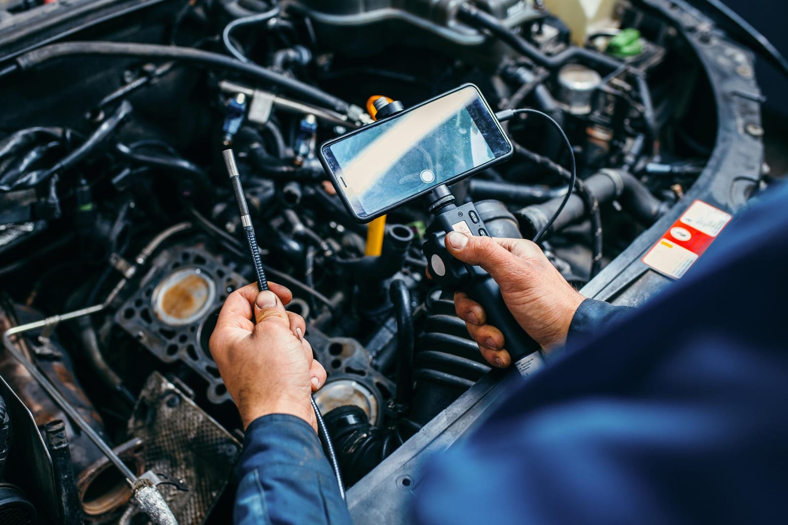 Mecânico usa uma câmera endoscópio conectada a um celular para inspecionar um motor aberto.